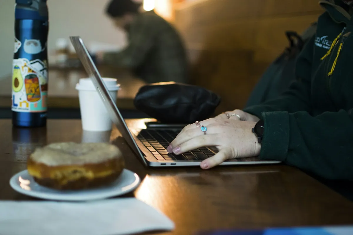 Person använder mobil bankapp på ett café med laptop bredvid
